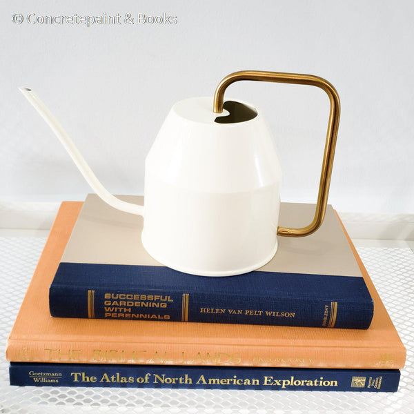 stack of hardcover coffee table books in blue and golden yellow with cream watering can. Real books and watering can as home decor.