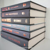 Stack of black and gray hardcover books with copper font. Real books staged and used as shelf décor.