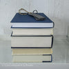 Stack of real hardcover books in navy blue and neutral colors. 