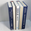 Stack of real hardcover books used as shelf décor in blues, white, and gray. Books on white ikea bookshelf.