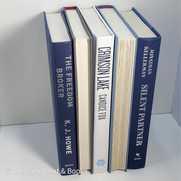 Stack of real hardcover books used as shelf décor in blues, white, and gray. Books on white ikea bookshelf.
